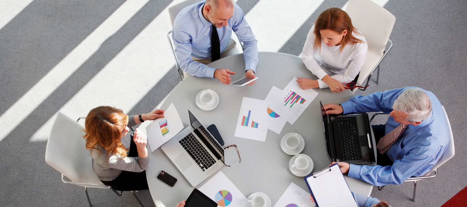 two corporate women and two corporate men sitting at a round table looking at paperwork