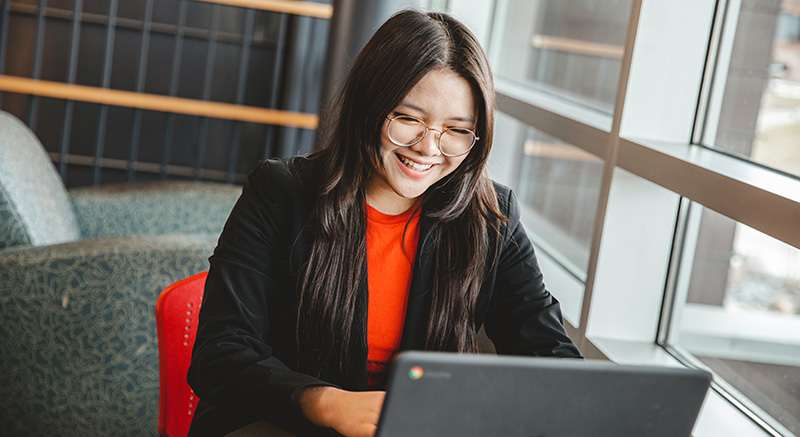 A Normandale student smiling at a computer screen.