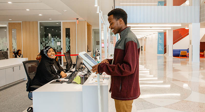 A student reviews information on a tablet, while a student services person looks on.