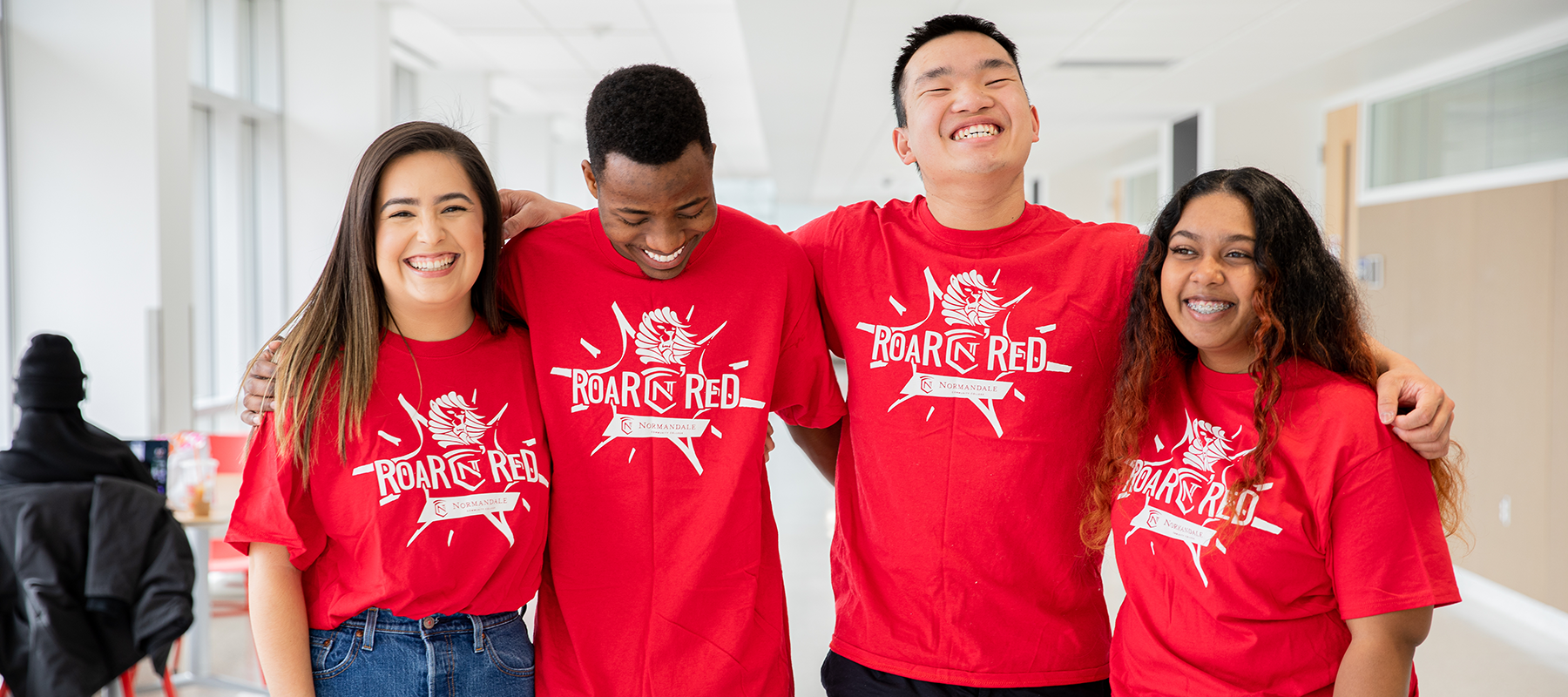 A diverse group of Normandale students in Roar N’ Red t-shirts smiling and laughing together. 